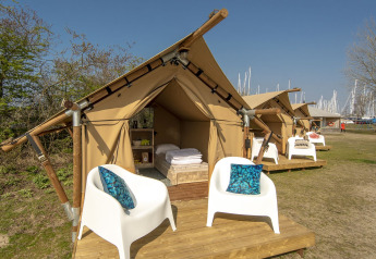 Safari tent at Marina Parcs Almere, Netherlands, featuring cozy setup, white chairs, and blue pillows outside.