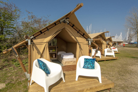 Tenda safari al Marina Parcs Almere, Paesi Bassi, con arredo accogliente, sedie bianche e cuscini blu all'esterno.