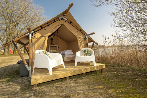 Tienda safari en Marina Parcs Almere, Países Bajos, con dos sillas blancas en una plataforma de madera junto al agua.