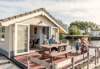 Gezin beleeft plezier op het terras van een chalet bij Marina Parcs Almere in Nederland, direct aan het water.