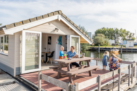 Gezin beleeft plezier op het terras van een chalet bij Marina Parcs Almere in Nederland, direct aan het water.