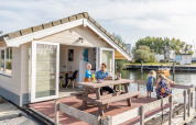 Familie nyder tid på terrassen foran chalet ved Chalets at Marina Parcs Almere, Holland, med udsigt til vandet.