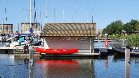 Red kayak by dock next to small lodge at Chalets at Marina Parcs Almere, Netherlands, sunny day.