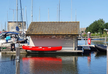 Red kayak by dock next to small lodge at Chalets at Marina Parcs Almere, Netherlands, sunny day.