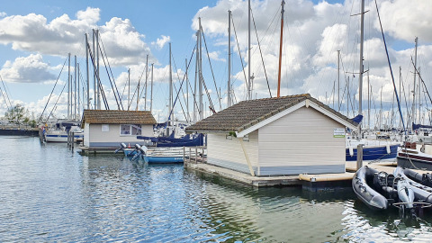 Floating chalets at Marina Parcs Almere in the Netherlands, surrounded by sailboats and a blue sky.