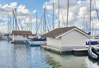 Floating chalets at Marina Parcs Almere in the Netherlands, surrounded by sailboats and a blue sky.