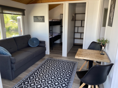 Interior de lodge moderno con sofá, mesa de comedor, literas y gran ventana en Marina Parcs Almere.