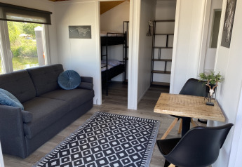 Interno moderno di chalet con divano grigio, tavolo da pranzo e letto a castello a Marina Parcs Almere.
