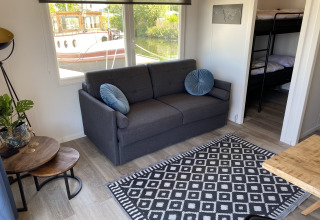 Living area with grey sofa, blue pillows, patterned rug, bunk beds and boat view at Chalets at Marina Parcs Almere.