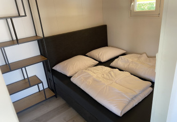 Piccola camera da letto con letto matrimoniale, scaffale e finestra, Chalets a Marina Parcs Almere nei Paesi Bassi.