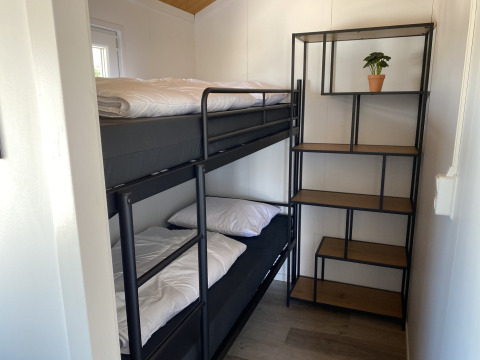 Habitación pequeña con litera y estantería con planta, en Chalets at Marina Parcs Almere, Países Bajos.