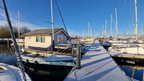 Boats and chalets at Marina Parcs Almere in the Netherlands with a sunny blue sky and frosty walkway.