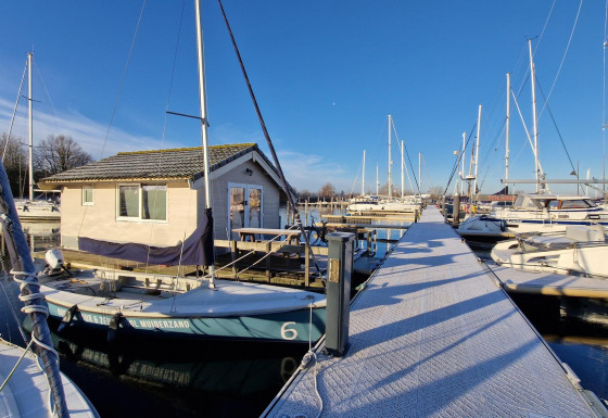 Boats and chalets at Marina Parcs Almere in the Netherlands with a sunny blue sky and frosty walkway.