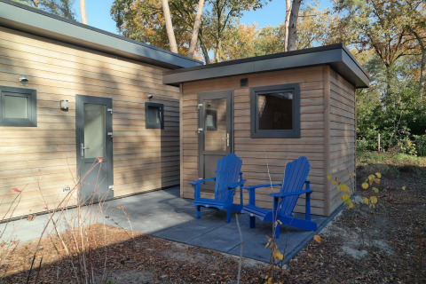 Area esterna del Forest park chalet 8p all’Holiday park De Kleine Belties con due sedie blu.