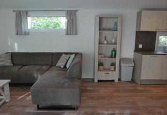 Living room in Forest park chalet 8p at Holiday park De Kleine Belties with sofa, shelving, and kitchen.