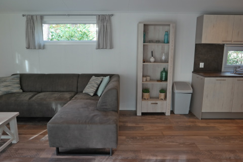 Living room in Forest park chalet 8p at Holiday park De Kleine Belties with sofa, shelving, and kitchen.