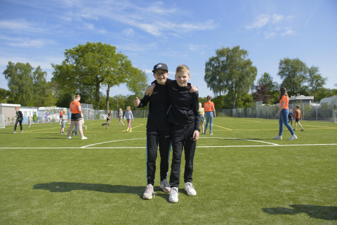 Due ragazzi su un campo da gioco in un alloggio glamping, circondati da altri bambini che giocano fuori.