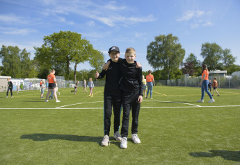 Due ragazzi su un campo da gioco in un alloggio glamping, circondati da altri bambini che giocano fuori.