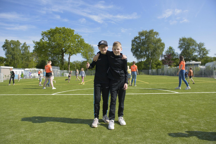Dos niños en un parque de una zona de glamping, rodeados de otros niños jugando al aire libre.