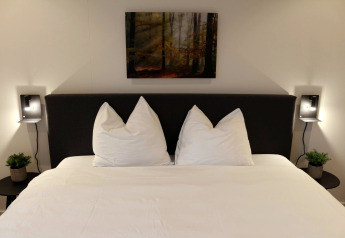 Lit moderne avec draps blancs, tables de chevet et lampes murales au Forest Cube, Holiday Park BreeBronne, Pays-Bas.