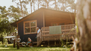 Gezin geniet buiten bij de Youpi! Lodge safaritent, omgeven door bos, zon en houten veranda.