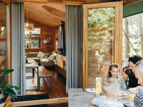 Familie nyder morgenmad udenfor en træhytte ved Youpi! Lodge på Beerze Bulten, Holland, med åbne døre.