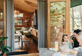 Familie nyder morgenmad udenfor en træhytte ved Youpi! Lodge på Beerze Bulten, Holland, med åbne døre.