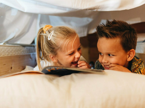 Dos niños leen y se ríen juntos bajo una manta en Youpi! Lodge, Beerze Bulten, Países Bajos.