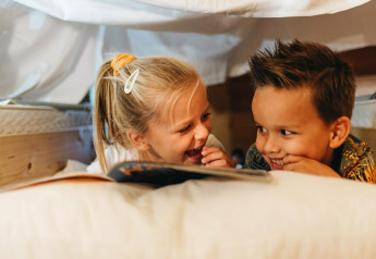 Due bambini leggono e ridono insieme sotto una coperta a Youpi! Lodge, Beerze Bulten, Paesi Bassi.