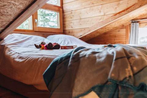 Cama acogedora con juguete y libro en un ático de madera en Youpi! Lodge, Beerze Bulten, Países Bajos.