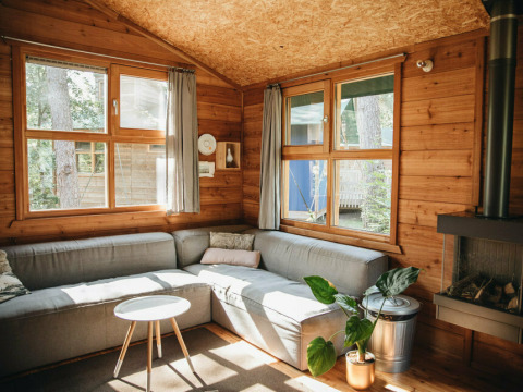 Hyggelig stue i en safari-telt-lodge med store vinduer, trævægge og moderne sofa i Beerze Bulten.