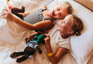 Dos niños sonrientes juegan en la cama dentro de una tienda safari en Youpi! Lodge en Beerze Bulten, Países Bajos.