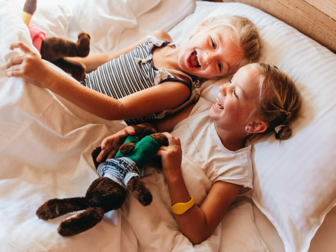 Twee gelukkige kinderen lachen en spelen in bed in een safaritent bij Youpi! Lodge op Beerze Bulten.