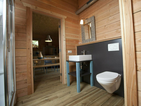 Baño revestido de madera con lavabo y WC de pared en Youpi! Lodge, Beerze Bulten, Países Bajos.