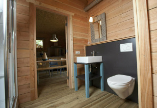 Badkamer met houten wanden, wastafel en hangtoilet in Youpi! Lodge bij Beerze Bulten, Nederland.