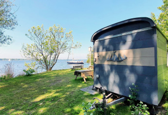 Kleines blaues Tiny House am See mit Bäumen, Gras und Boot, Tiny Wagon bei Marina Parcs Almere, Niederlande.