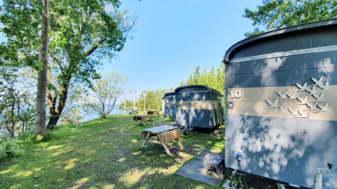 Piccole case vicino al lago a Marina Parcs Almere, Paesi Bassi, tra alberi e tavoli da picnic.