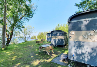 Piccole case vicino al lago a Marina Parcs Almere, Paesi Bassi, tra alberi e tavoli da picnic.