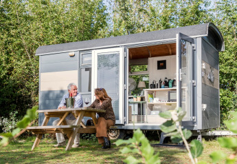 Due persone sedute fuori dalla Tiny Wagon al Marina Parcs Almere, Paesi Bassi, godendosi la natura.