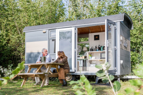 Dos personas sentadas fuera de la Tiny Wagon en Marina Parcs Almere, Países Bajos, disfrutando del día.