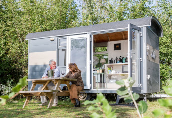 Due persone sedute fuori dalla Tiny Wagon al Marina Parcs Almere, Paesi Bassi, godendosi la natura.