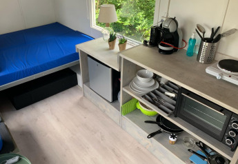 Kompakt interiør i Tiny Wagon, Marina Parcs Almere, Nederlandene med seng, tekøkken og vindue.