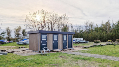 Casa pequeña llamada Tiny Wagon en Marina Parcs Almere, Países Bajos, rodeada de césped y barcos.