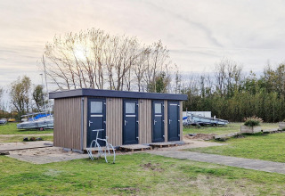 Casa pequeña llamada Tiny Wagon en Marina Parcs Almere, Países Bajos, rodeada de césped y barcos.