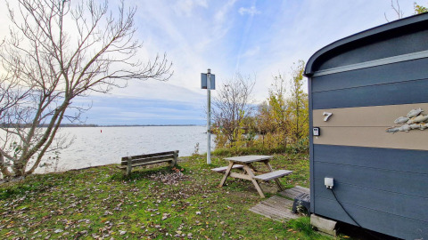 Vista lago dal Tiny Wagon di Marina Parcs Almere, panchina e tavolo da picnic tra alberi autunnali.