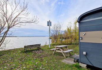 Vista lago dal Tiny Wagon di Marina Parcs Almere, panchina e tavolo da picnic tra alberi autunnali.