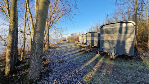 Små hytter kaldet Tiny Wagon ved Marina Parcs Almere i Holland, omgivet af træer og frost på jorden.