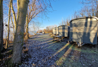 Små hytter kaldet Tiny Wagon ved Marina Parcs Almere i Holland, omgivet af træer og frost på jorden.