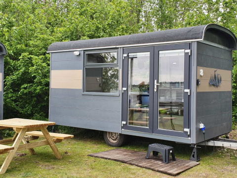 Casa pequeña Tiny Wagon en Marina Parcs Almere, Países Bajos, con mesa de picnic y vegetación alrededor.