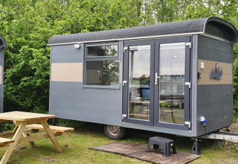 Et lille Tiny Wagon-hus ved Marina Parcs Almere i Holland med bordbænkesæt foran og græs omkring.